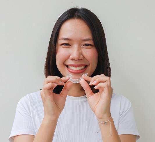 Woman smiling while holding Invisalign clear aligner