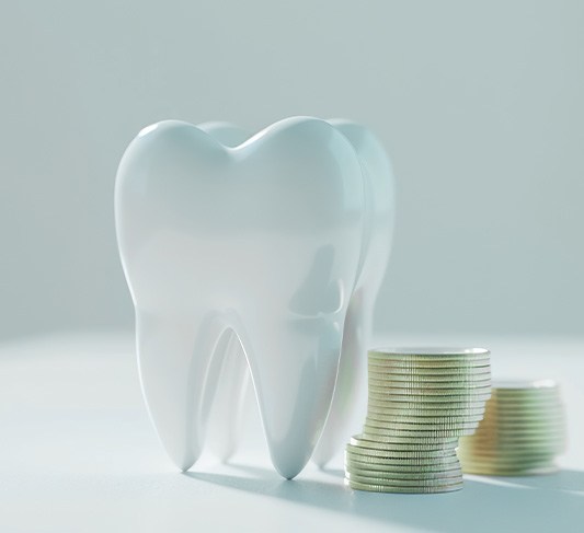 Large model tooth next to a pile of coins on a white surface with a white background