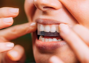 Nose-to-chin view of someone applying a whitening strip to their upper teeth